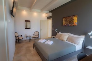 Habitación de hotel con cama, dos sillones, un escritorio, televisor de pantalla plana en la pared y un cuadro sobre la cama.