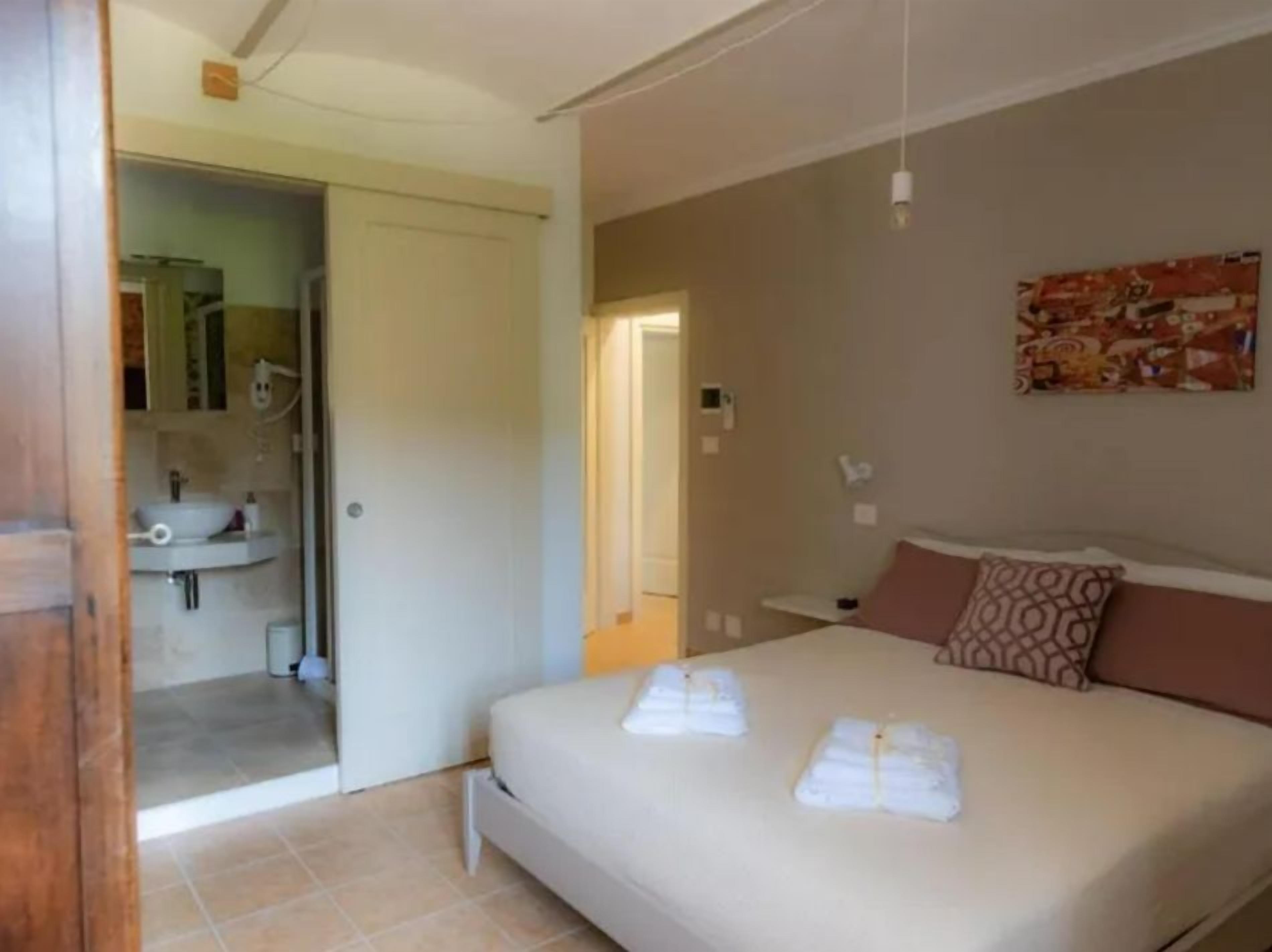 A bedroom with a bed, a bathroom visible through an open door, and a painting on the wall.