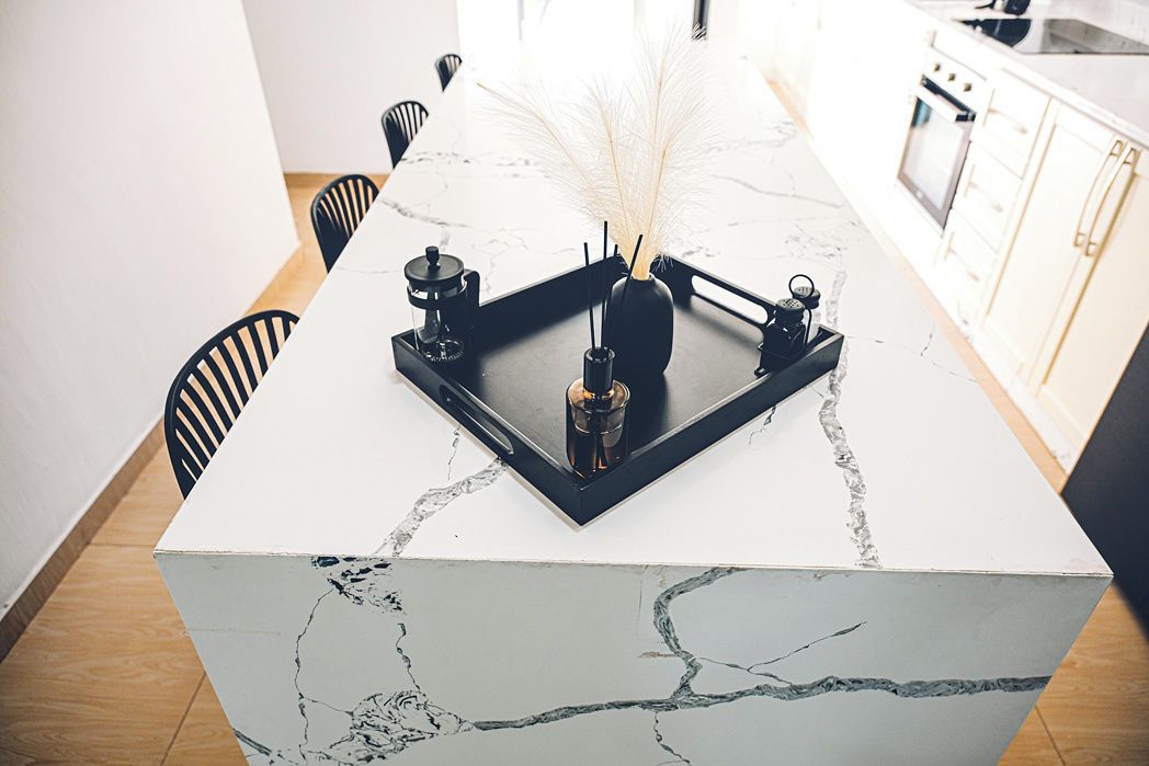 A kitchen island with a marble countertop, a black frame, and a vase with feathers.