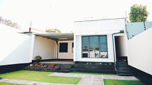 Et moderne hus i to etager med en overdækket terrasse, en lille have og en tydelig trappe til øverste etage.