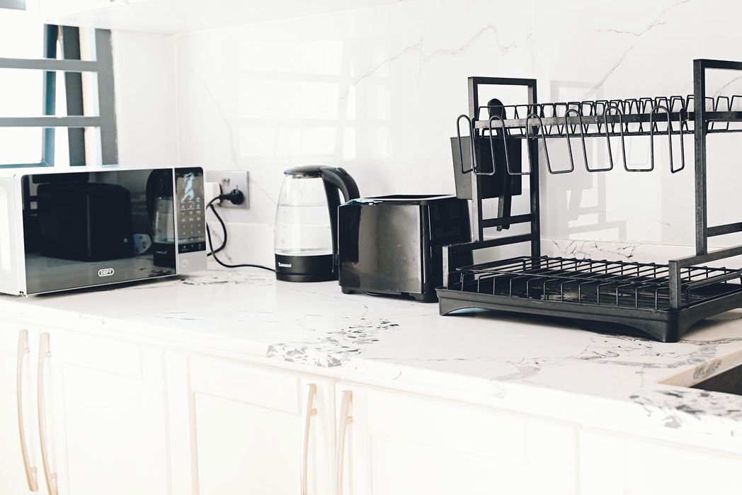 A kitchen with a microwave, coffee maker, and a black rack with hooks.