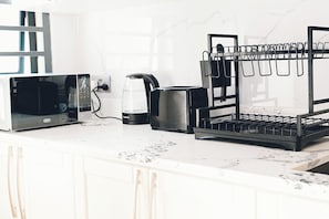 Una cucina con forno a microonde, macchina del caffè e un mobiletto nero con ganci.