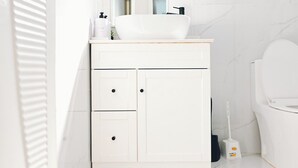 Et badeværelse med et hvidt underskab, en vask, et spejl og et toilet.