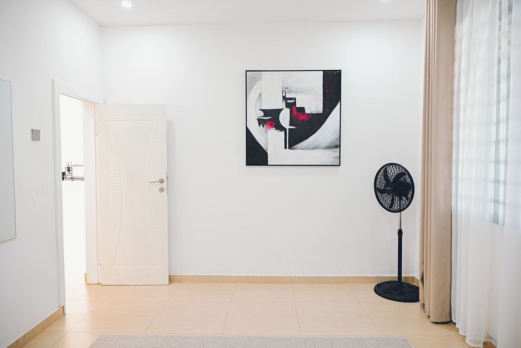 A room with a white door, a standing fan, and a wall-mounted abstract painting.