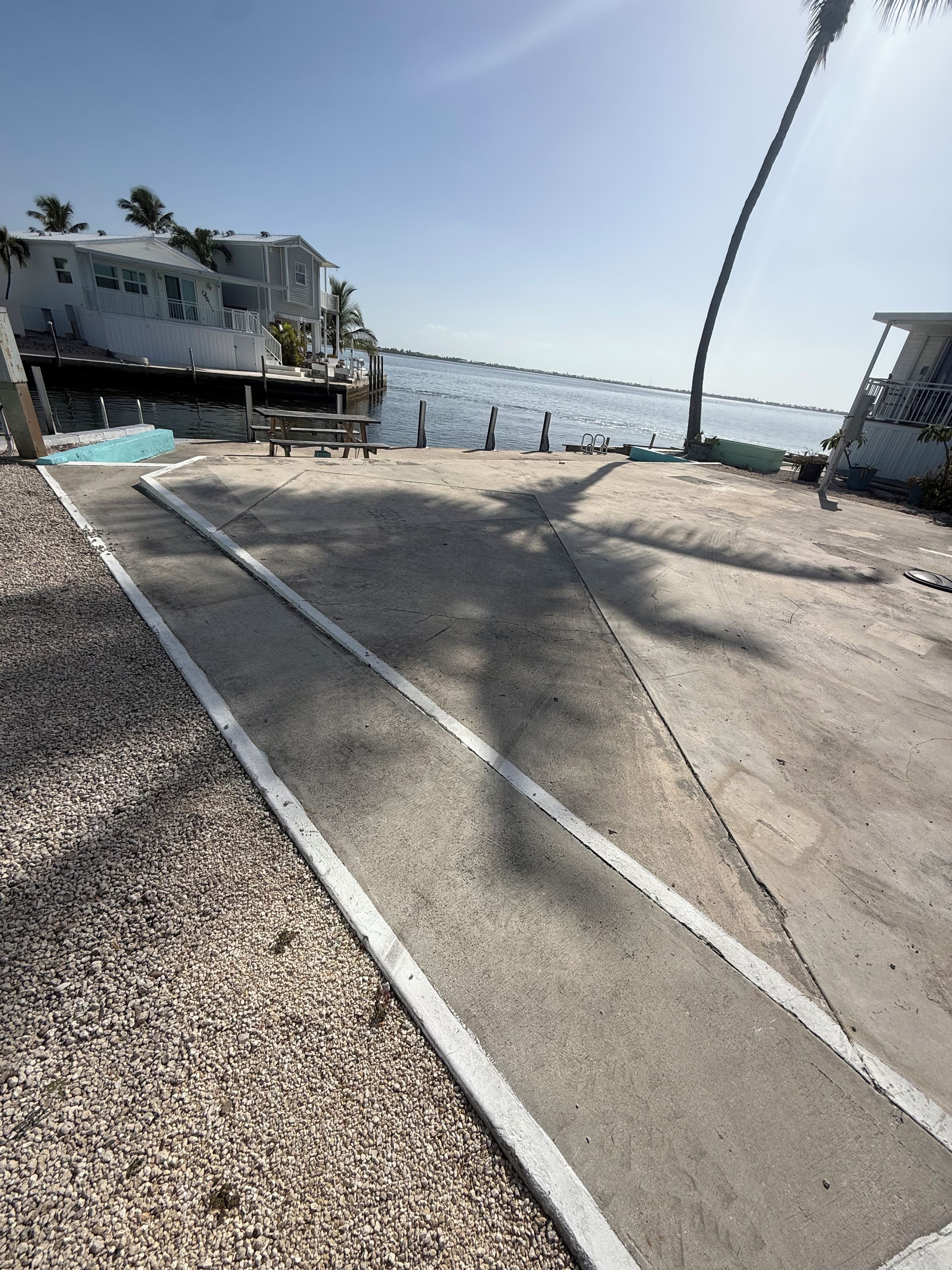 Caminho de concreto que leva a uma área à beira-mar, com um banco e uma mesa pequena.