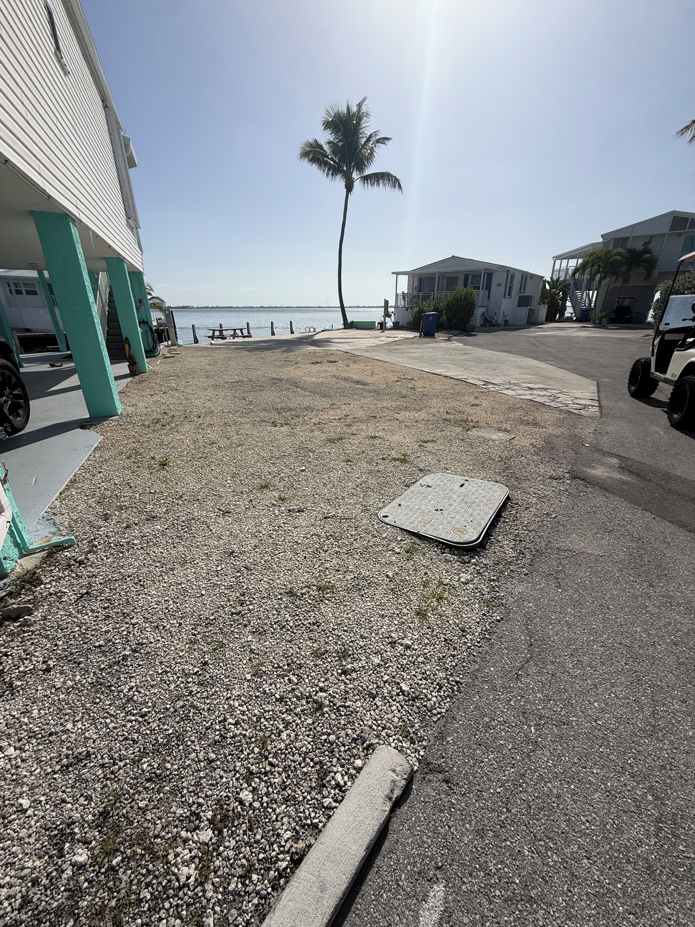 A gravel area with a manhole cover, a palm tree, and a building with a balcony.