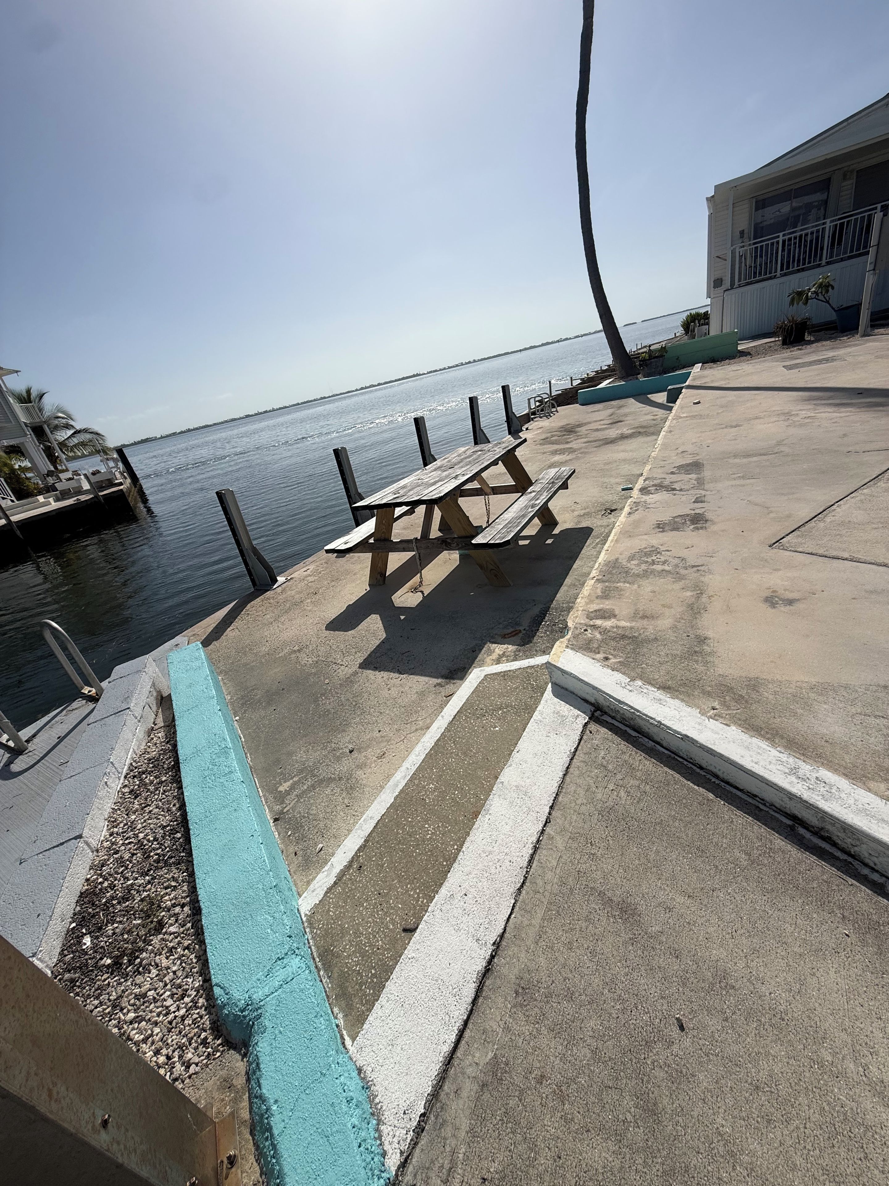 Een betonnen terras met een picknicktafel, een metalen hekwerk en uitzicht op het water.