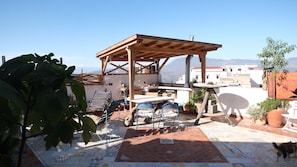 Una terraza en la azotea con una pérgola de madera, mobiliario exterior y plantas en macetas.