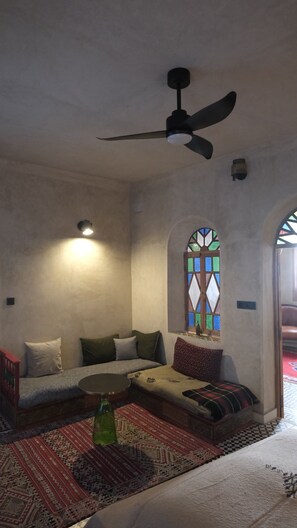 Una habitación con ventilador de techo, sofá, alfombra estampada y una ventana de vitral.