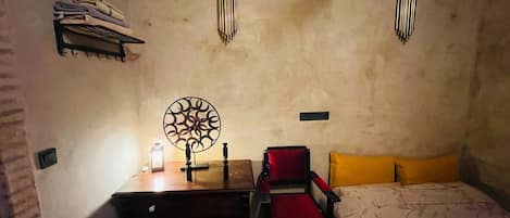 Quarto com cama, escrivaninha com abajur, cadeira e prateleira na parede com toalhas dobradas.