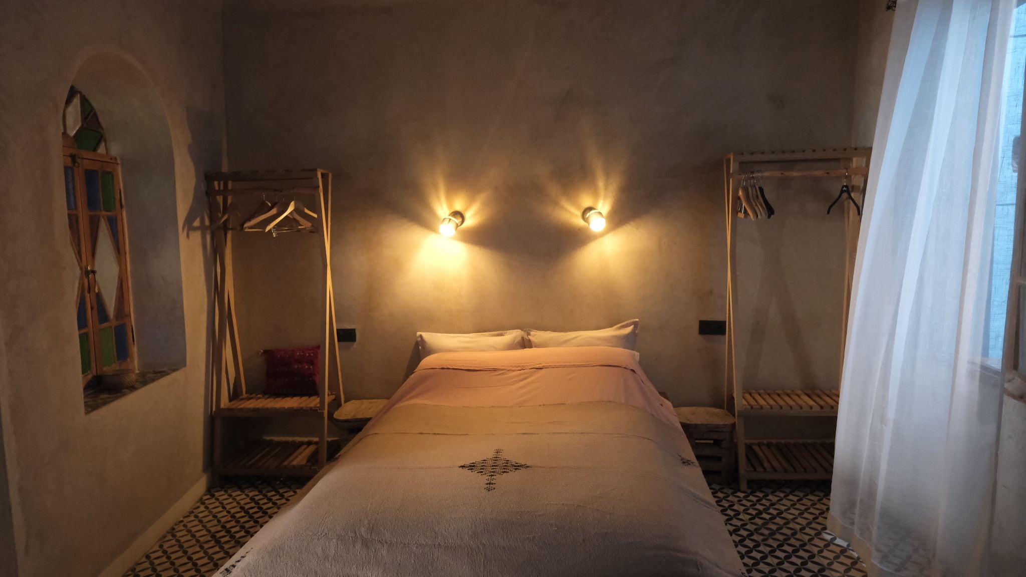 Une chambre à coucher comprenant un lit, deux lampes fixées au mur, une armoire et un portant à vêtements.