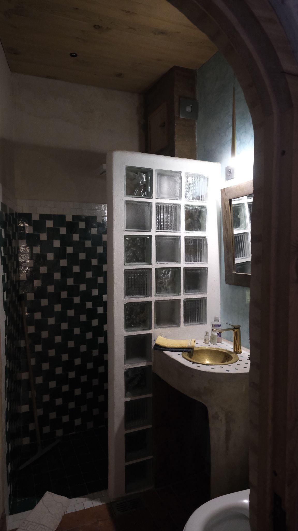 A bathroom with a tiled floor, a sink with a gold faucet, and a window with a view of the outside.