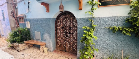 A traditional building with a patterned door, a wooden bench, and potted plants.