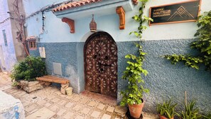 Un edificio tradicional con una puerta decorada, un banco de madera y plantas en macetas.