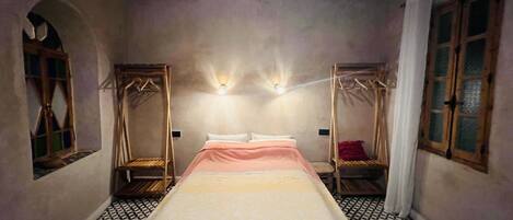 A room with a bed, two wall-mounted lights, a window with a curtain, and a patterned floor.
