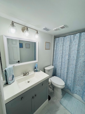 Une salle de bain avec un lavabo blanc, un miroir, des toilettes et un rideau de douche à motifs floraux.