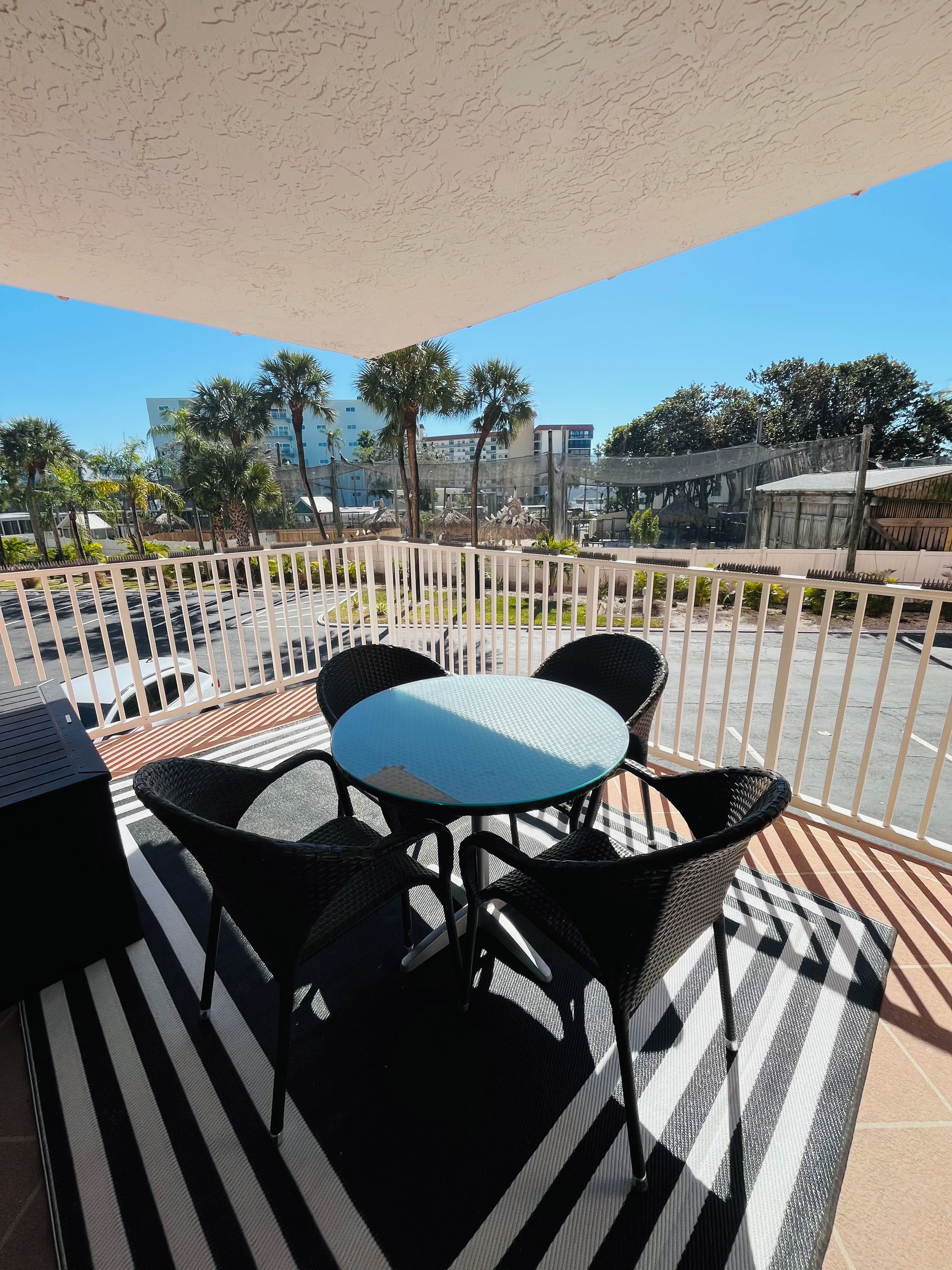Ein Balkon mit Tisch und Stühlen, einem gestreiften Boden und Blick auf Gebäude und Bäume.