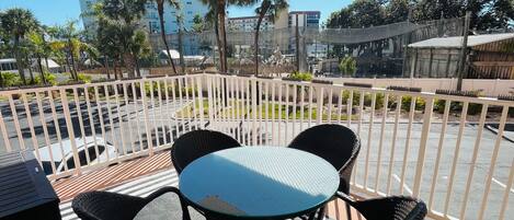 Un balcón con mesa y sillas, piso a rayas, y vistas a edificios y árboles.