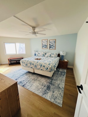 Une chambre à coucher avec un lit, un ventilateur de plafond, une table de chevet, une lampe et une fenêtre.