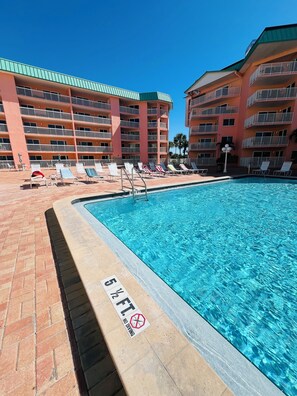 Une piscine avec des chaises longues et un panneau indiquant : « PROFONDEUR : 1,5 MÈTRE. INTERDIT DE SE NOYER ».