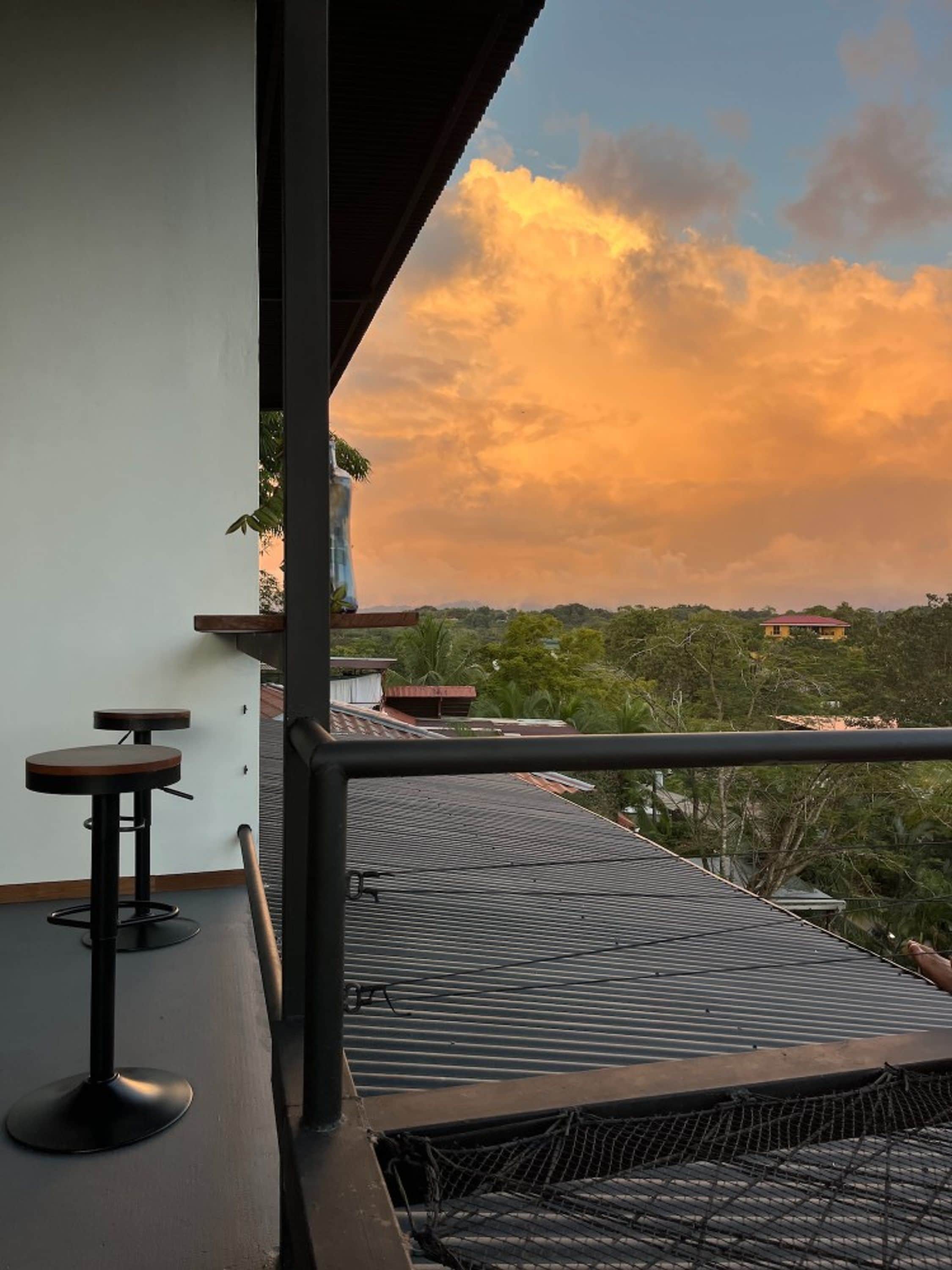 Varanda com vista para o pôr do sol, corrimão e dois banquetes.