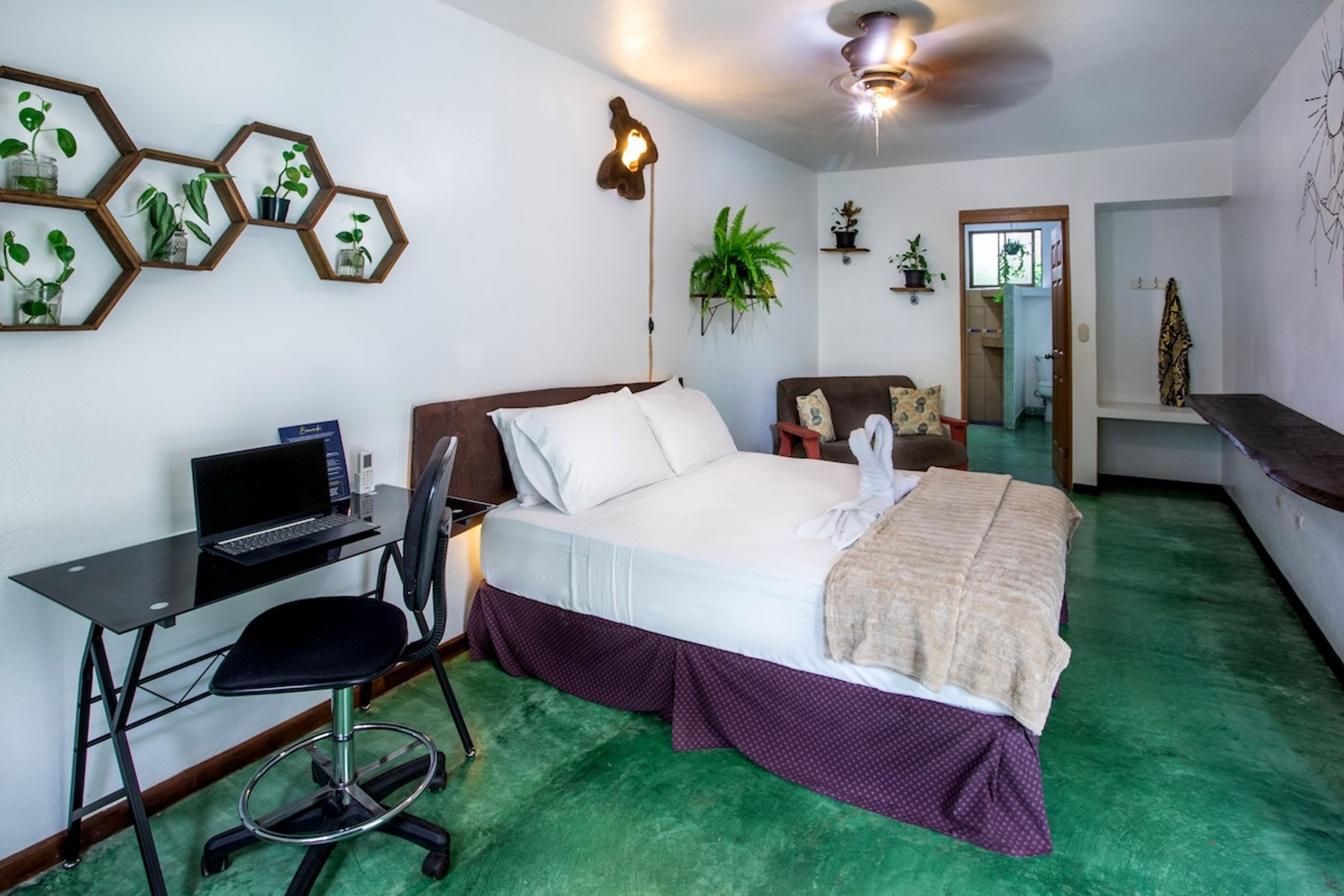 Habitación de hotel con cama, escritorio, silla y ventilador de techo.