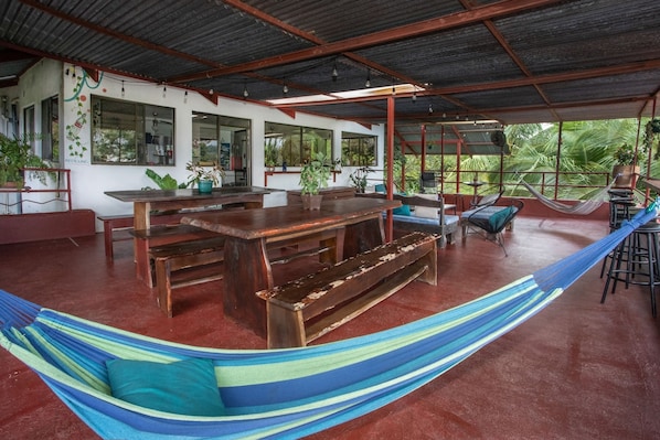 A spacious indoor area with a large wooden table, benches, and a hammock.