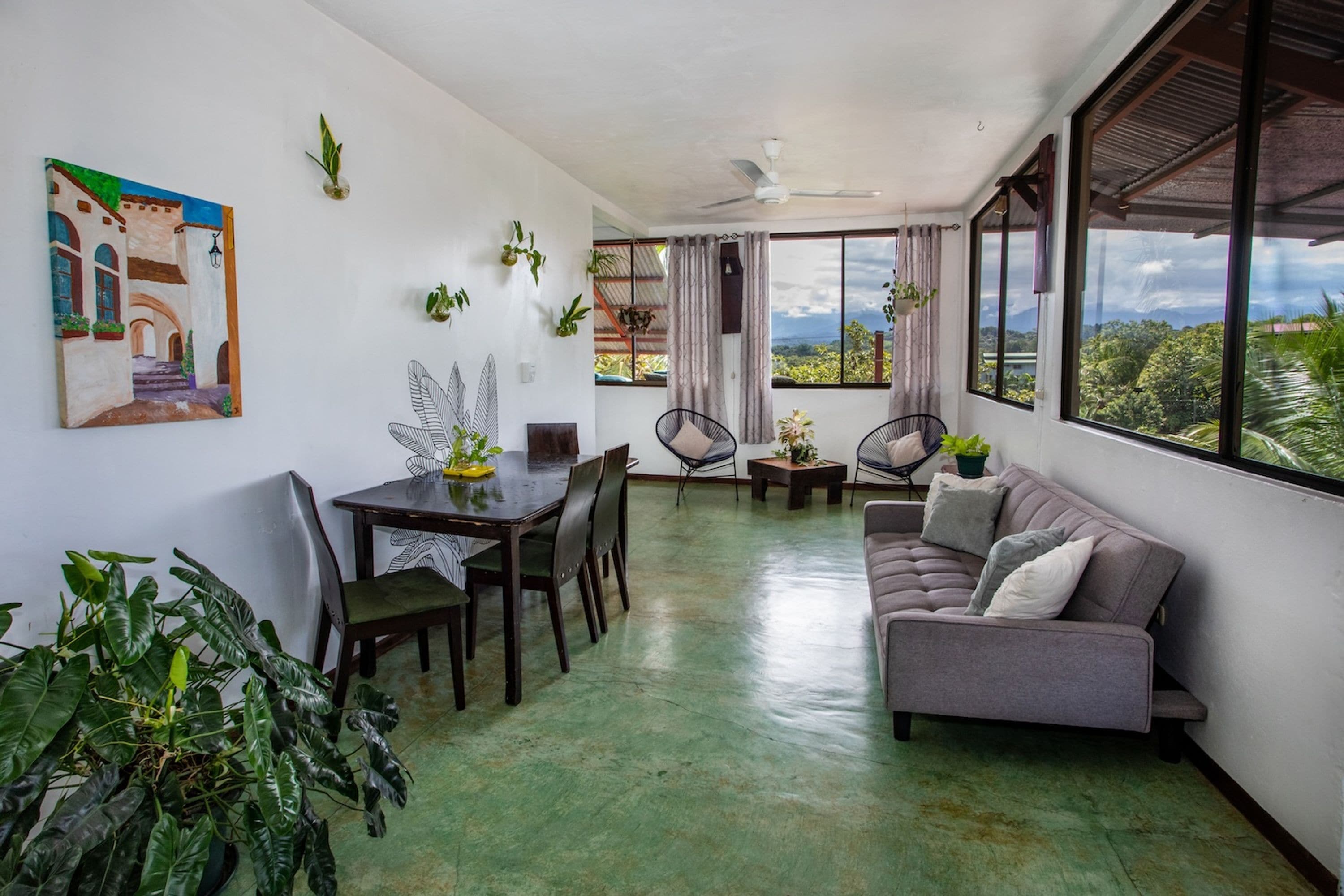 A spacious living area with a dining table, chairs, a sofa, and a view of the outdoors.