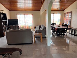 Una sala de estar con sofá, televisión y comedor con sillas y mesa.