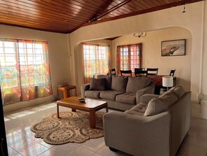 A living room with a sofa, a coffee table, and a dining area with chairs and a table. - Spacious 4-bedroom house in tranquil St Croix with AC (St Croix)
