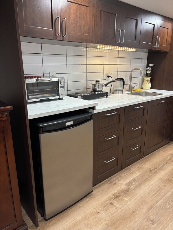 A modern kitchen with dark wooden cabinets, a built-in dishwasher, a stainless steel toaster oven, and a sink with a faucet. - Cozy East York Suite | Private & Quiet | Close to Transit (Toronto)