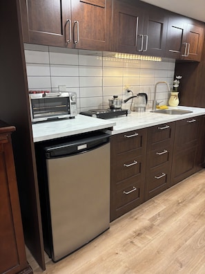 A modern kitchen with dark wooden cabinets, a built-in dishwasher, a stainless steel toaster oven, and a sink with a faucet.