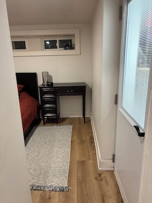 Quarto com cama, escrivaninha, tapete e janela com persianas.