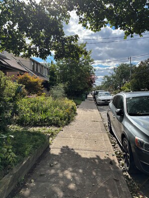 A residential street with parked cars, a sidewalk, and houses with visible windows and roofs. - Cozy East York Suite | Private & Quiet | Close to Transit (Toronto)