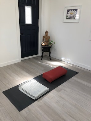 A room with a black mat, a red cushion, a Buddha statue, and a framed picture on the wall.