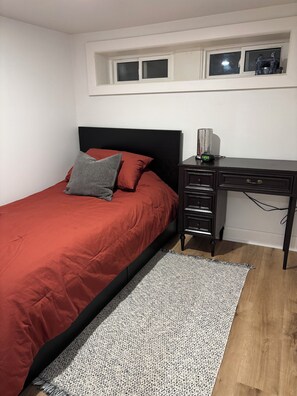 A bedroom with a bed, a desk, and a window.