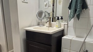 Un bagno con un lavandino bianco, uno specchio, un mobile scuro, una doccia e un asciugamano appeso al muro.