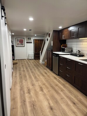 A modern kitchen with wooden flooring, dark cabinets, and a white countertop. - Cozy East York Suite | Private & Quiet | Close to Transit (Toronto)