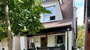 Una casa a due piani con un portico, il numero '153½' ben visibile, e un piccolo giardino.