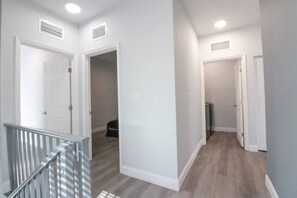 A hallway with white walls, a grey floor, and a metal railing. There are two doors and a small closet with a radiator. - Sleek Modern Townhome Shared Backyard Oasis (Miami)