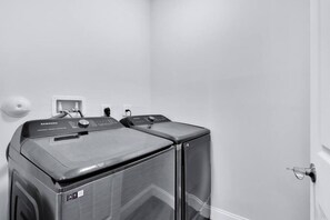 A laundry room with a Samsung washer and dryer, a white wall, and a door. - Sleek Modern Townhome Shared Backyard Oasis (Miami)