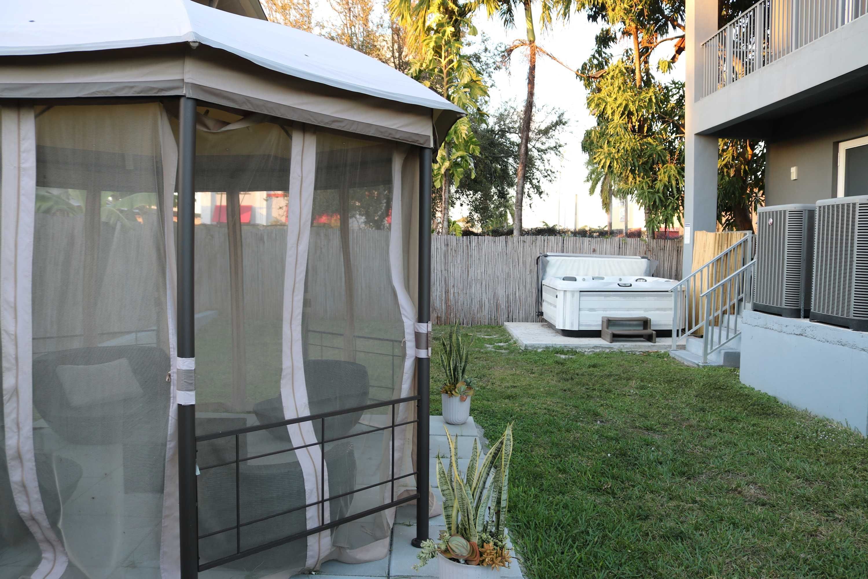 A covered patio area with a screened enclosure, a hot tub, and a grassy yard.