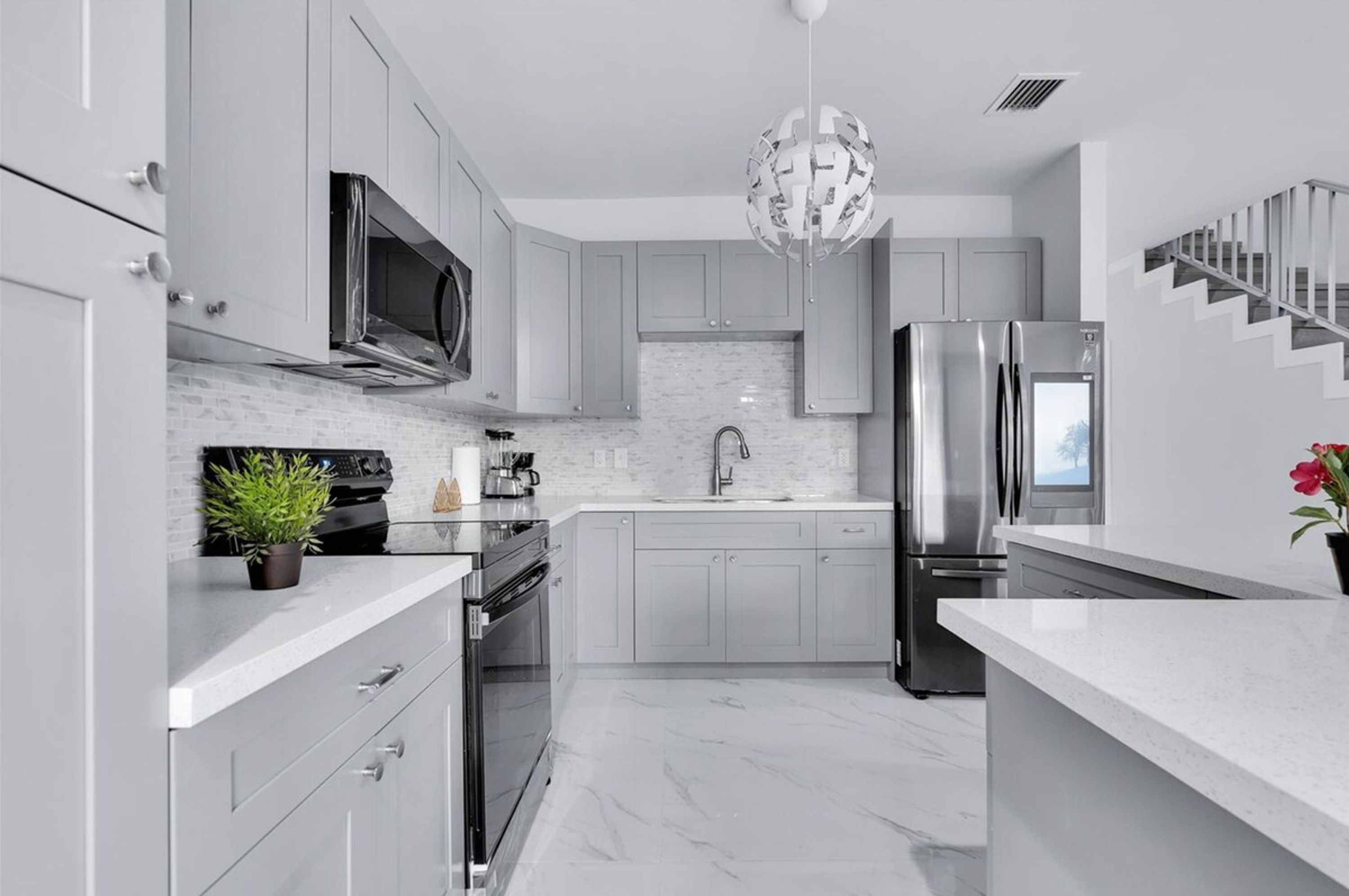 A modern kitchen with grey cabinetry, stainless steel appliances, a marble countertop, and a unique spherical pendant light.