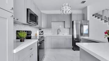 Cozinha moderna com armários cinza, eletrodomésticos de aço inoxidável, bancada de mármore e uma luminária pendente esférica singular.