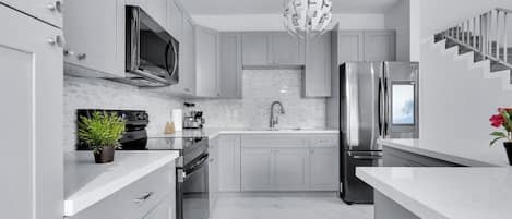 Una cocina moderna con armarios grises, electrodomésticos de acero inoxidable, encimera de mármol y una lámpara colgante esférica original.
