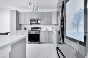 A modern kitchen with grey cabinets, a built-in oven, a microwave, and a large refrigerator. - Sleek Modern Townhome Shared Backyard Oasis (Miami)