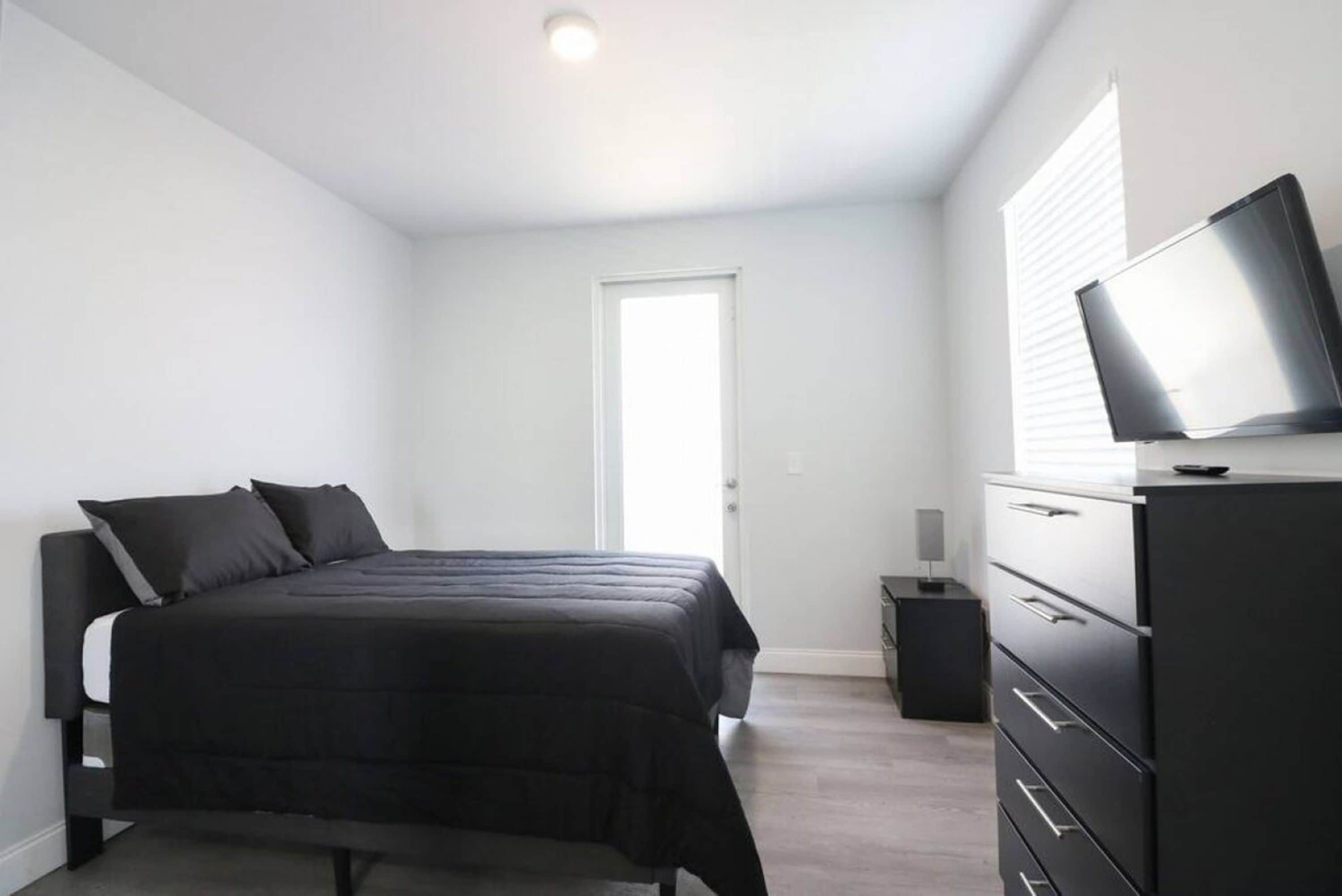 A bedroom with a bed, a dresser, a television, and a door.