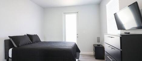A bedroom with a bed, a dresser, a television, and a door.