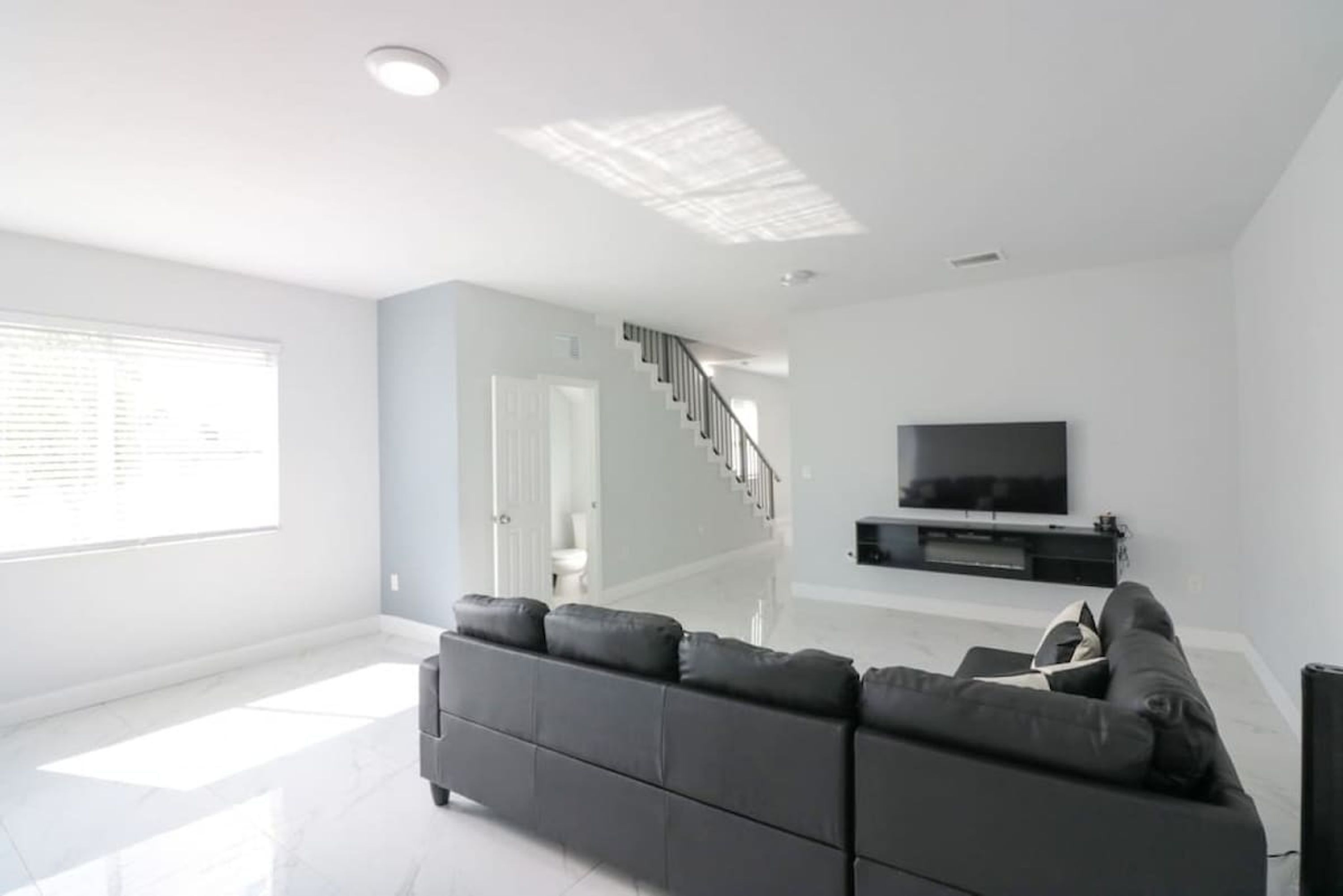 Uma sala de estar moderna com um sofá cinza, uma TV de tela plana e uma escada que leva a outro cômodo.