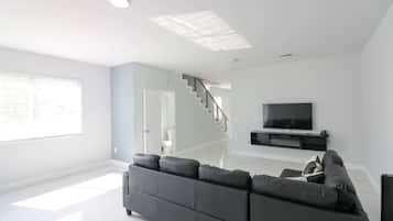 Uma sala de estar moderna com um sofá cinza, uma TV de tela plana e uma escada que leva a outro cômodo.